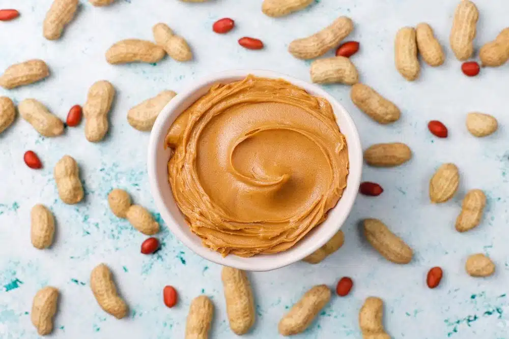 Peanut butter in a bowl surrounded by peanuts for weight loss