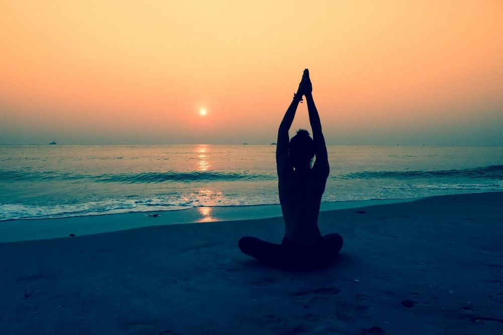 Woman meditating on beach at sunset for 8 Dimensions of Wellness, theory wellness, emotional wellness, spiritual wellness