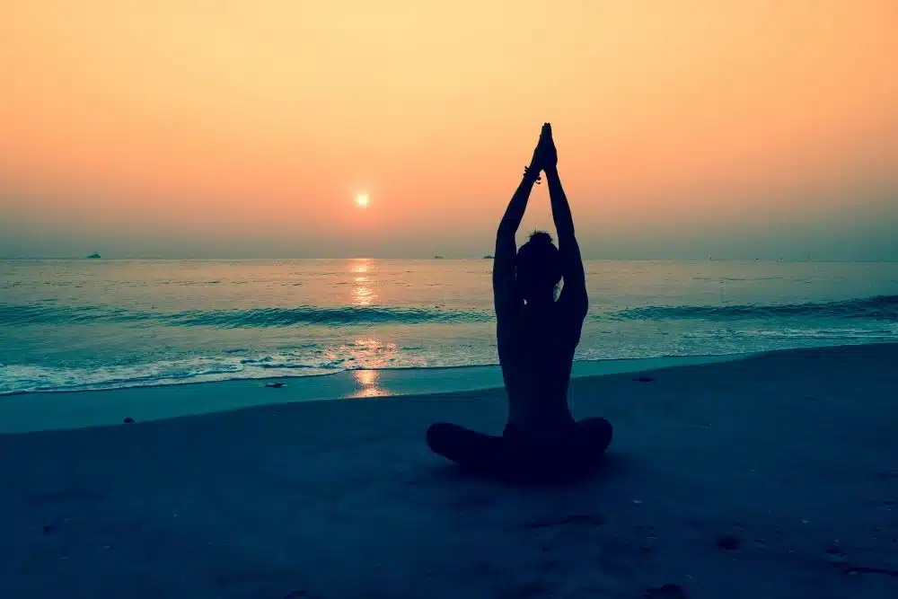 Woman meditating on beach at sunset for 8 Dimensions of Wellness, theory wellness, emotional wellness, spiritual wellness