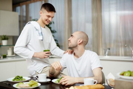 2 men in kitchen, one eating green veg and other serving, Bone marrow transplant recovery, cancer nutrition
