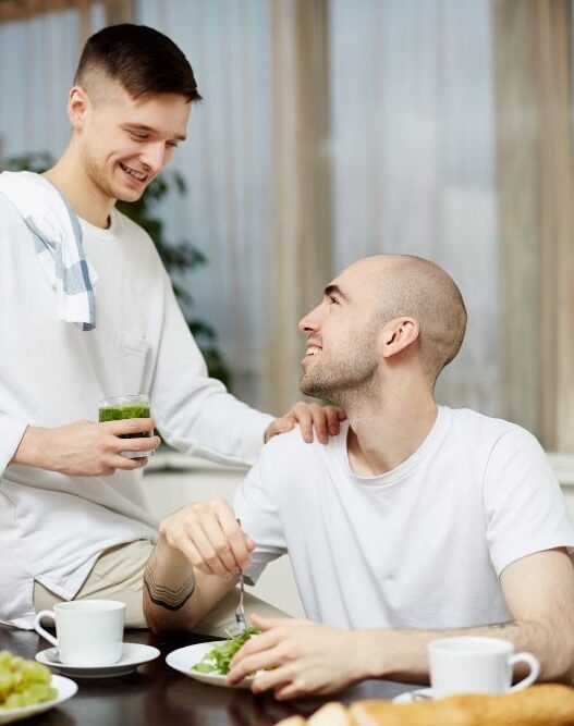 2 men in kitchen, one eating green veg and other serving, Bone marrow transplant recovery, cancer nutrition