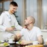 2 men in kitchen, one eating green veg and other serving, Bone marrow transplant recovery, cancer nutrition