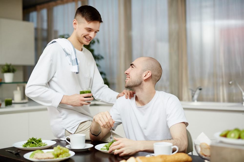 2 men in kitchen, one eating green veg and other serving, Bone marrow transplant recovery, cancer nutrition