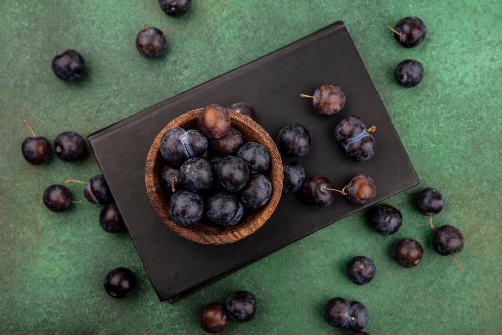 Kala Jamun or Black plum in a bowl, some on tray and some on green mat