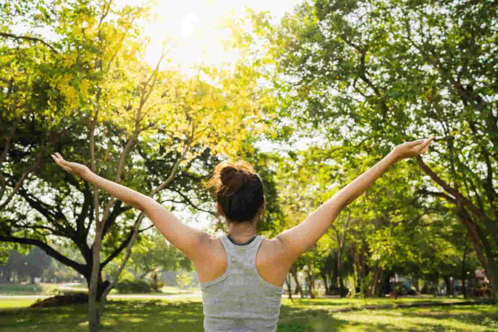 Woman in garden with sunlight raising arms to show the superpower of self, the power of your subconscious mind