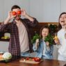 man, woman, child in kitchen showing healthy fruits and vegetables